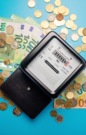 compteur électrique posé sur plusieurs billets de 100€ et des pièces d'argent