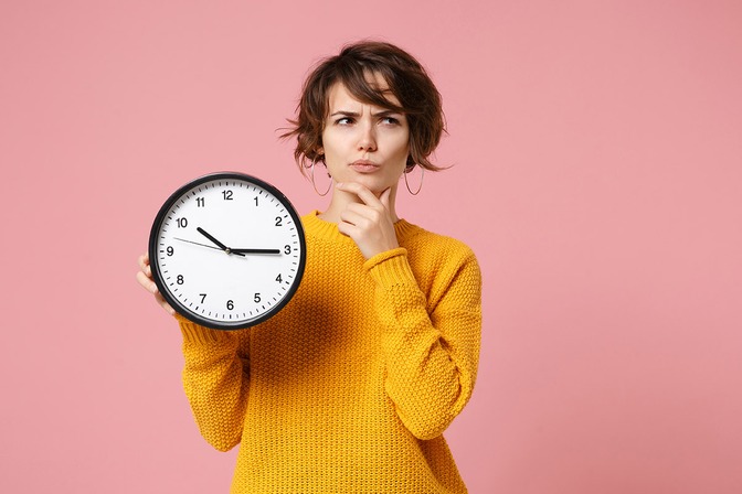une femme réfléchit avec une horloge en main fond rose