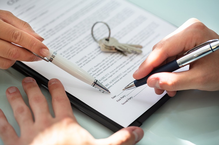 une personne signe un document un stylo d'une autre personne pointe un endroit du document trousseau de clés sur le document